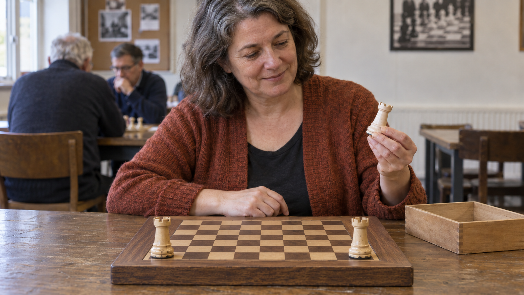 A chess club member compares an extra pale rook with two worn rooks on a wooden board