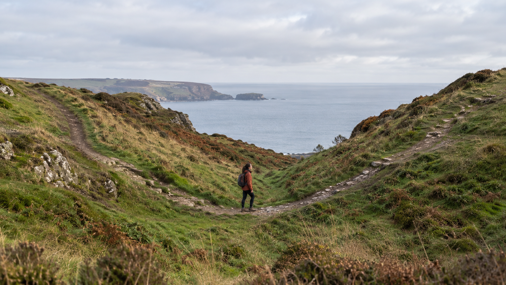 A hiker pauses where a coastal path descends into a hollow before climbing the opposite slope